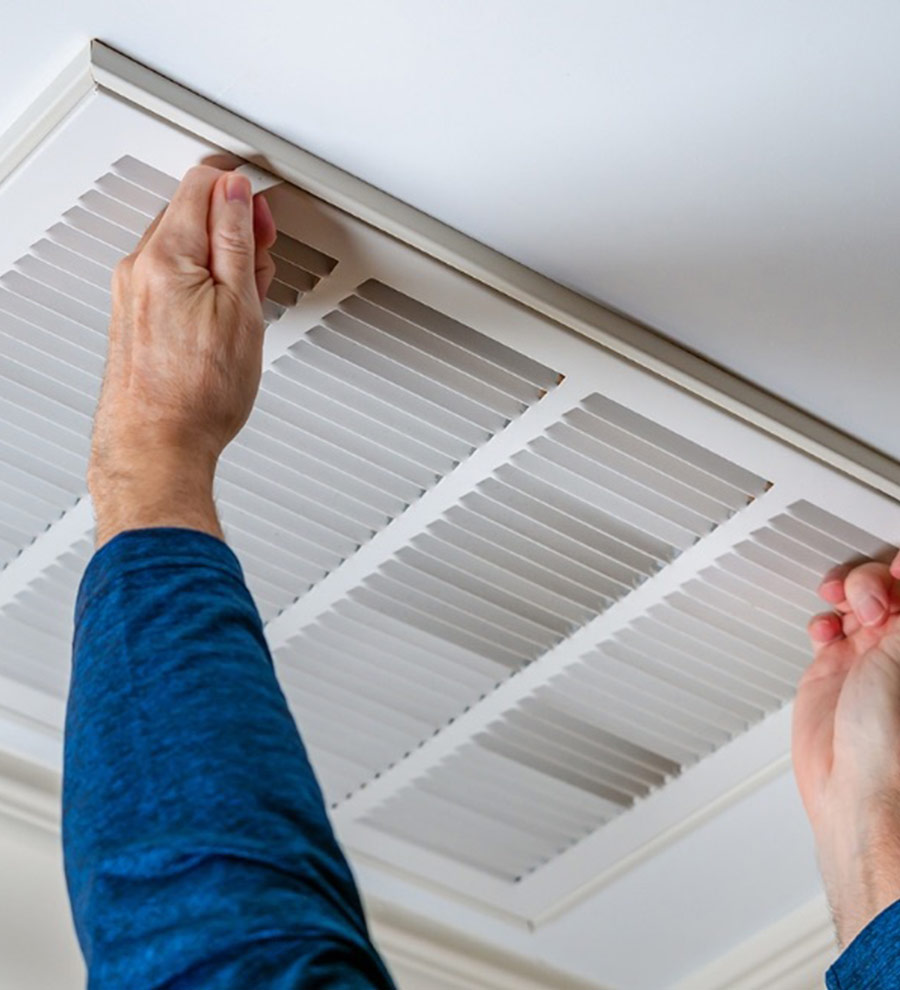 Mains d'une personne retirant une grille de ventilation au plafond pour nettoyage ou entretien, illustrant l'importance de l'entretien régulier des systèmes de ventilation domestiques.